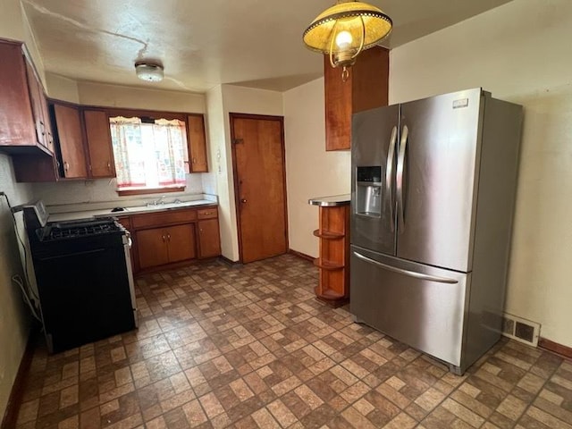 kitchen featuring visible vents, brown cabinets, range with gas cooktop, stainless steel fridge with ice dispenser, and baseboards