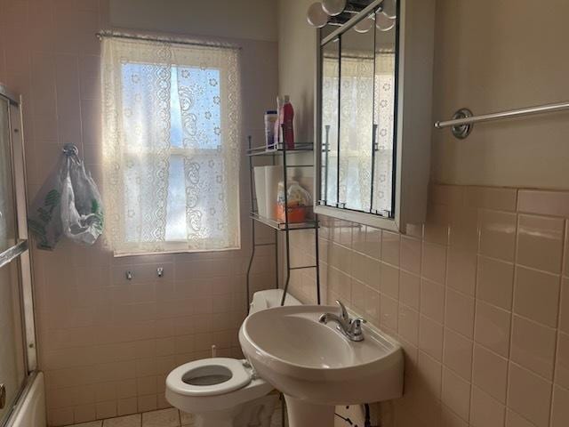 full bathroom featuring toilet, shower / bath combination with glass door, tile patterned floors, tile walls, and a sink