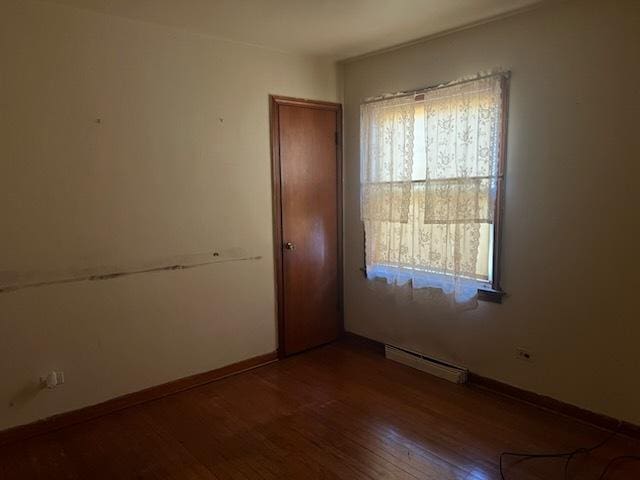 unfurnished room featuring baseboard heating, baseboards, and wood finished floors