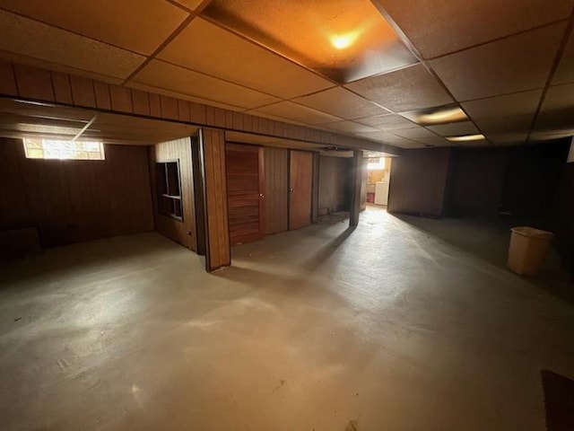 basement featuring wood walls and a drop ceiling