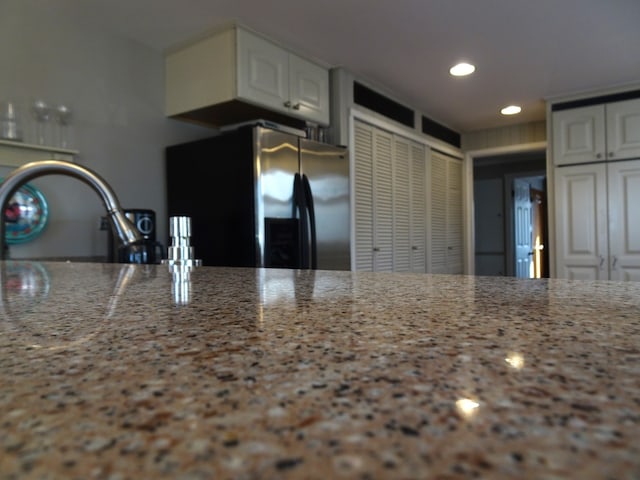 kitchen with a sink, light stone countertops, refrigerator with ice dispenser, and white cabinets