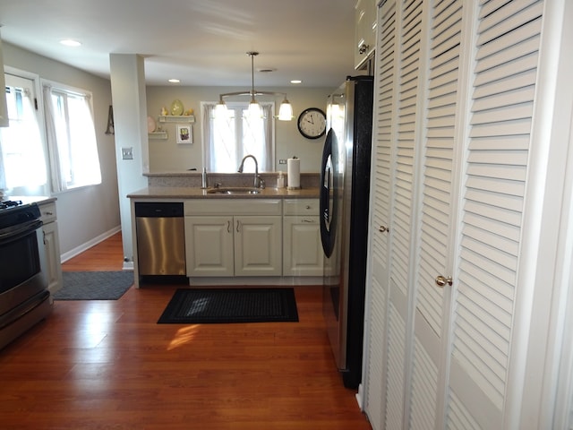 kitchen with wood finished floors, a sink, stainless steel appliances, white cabinets, and decorative light fixtures