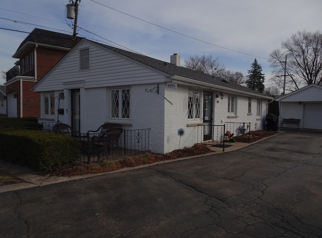 view of front of property featuring an outbuilding, a garage, brick siding, and a chimney