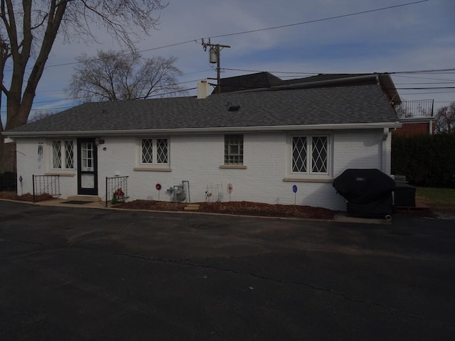 view of front of property with brick siding, roof with shingles, and a chimney