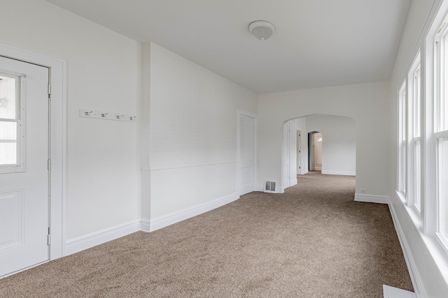 carpeted spare room with arched walkways, visible vents, and baseboards