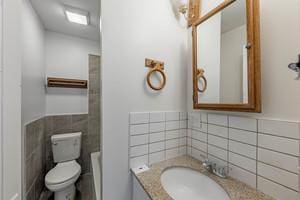 bathroom with tile walls, wainscoting, vanity, and toilet