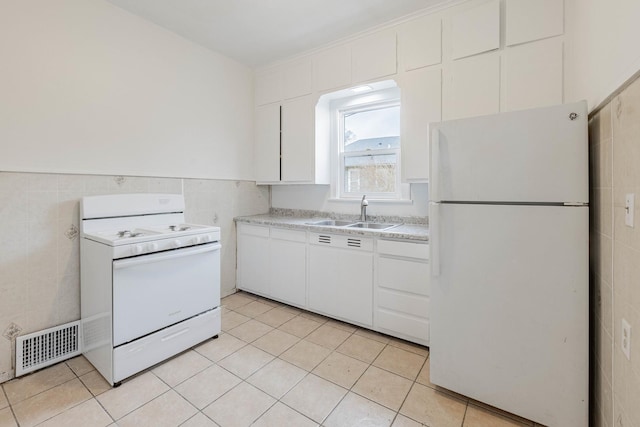 kitchen with white appliances, visible vents, a sink, and tile walls