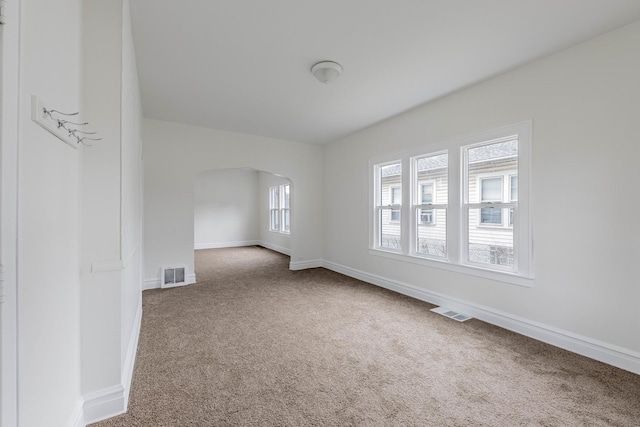 spare room featuring arched walkways, carpet floors, visible vents, and baseboards