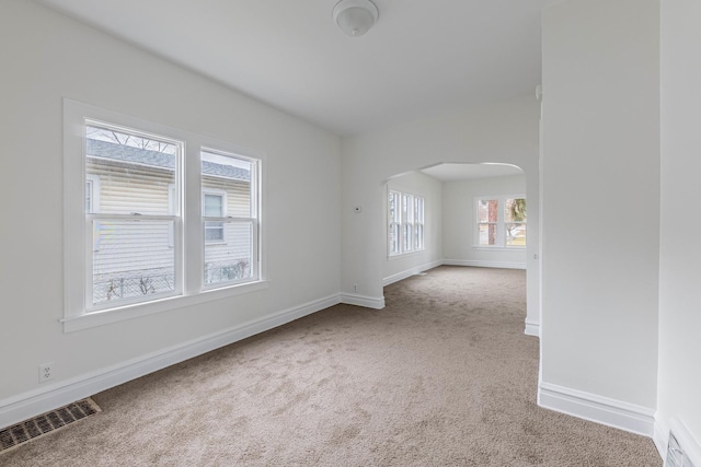 carpeted empty room featuring arched walkways, visible vents, and baseboards