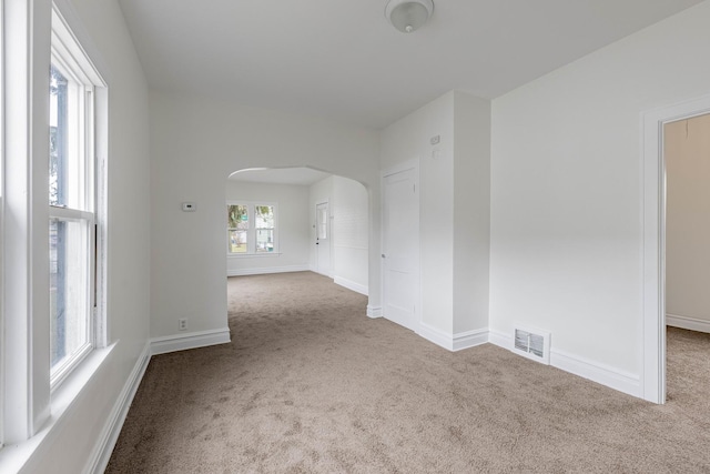 carpeted empty room featuring arched walkways, visible vents, and baseboards