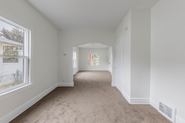 spare room featuring baseboards, visible vents, arched walkways, and carpet flooring