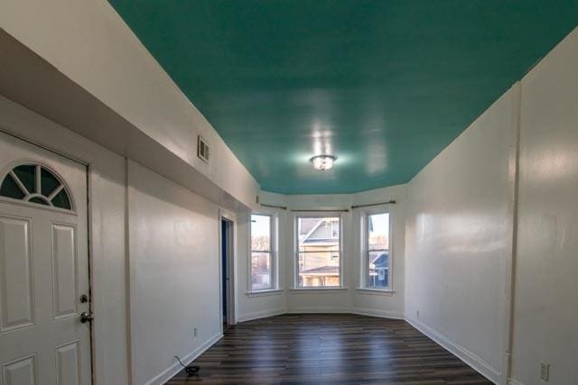 unfurnished room with dark wood-type flooring, visible vents, and baseboards