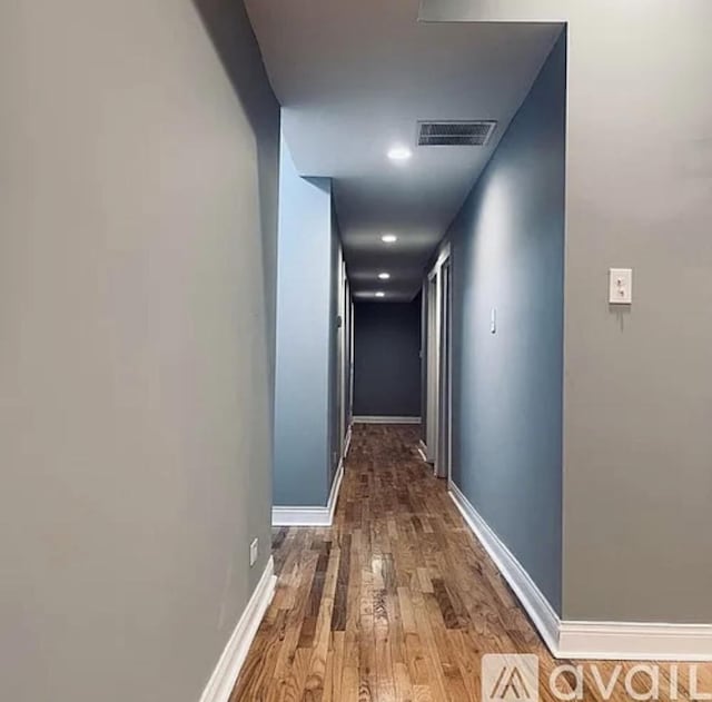 hall with visible vents, baseboards, and wood finished floors