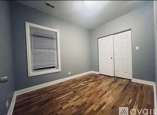 unfurnished bedroom featuring dark wood-style floors, baseboards, visible vents, and a closet