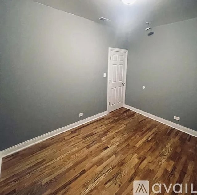 unfurnished room featuring dark wood-style flooring, visible vents, and baseboards