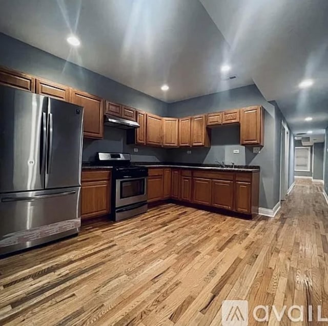 kitchen featuring light wood-style floors, dark countertops, brown cabinets, stainless steel appliances, and under cabinet range hood