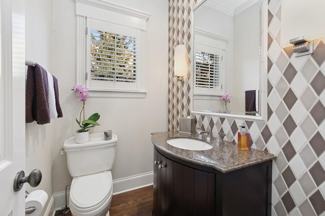 half bathroom featuring toilet, ornamental molding, vanity, wood finished floors, and baseboards