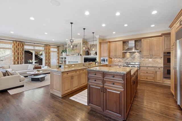 kitchen featuring wall chimney exhaust hood, appliances with stainless steel finishes, open floor plan, dark wood-style flooring, and a kitchen island with sink