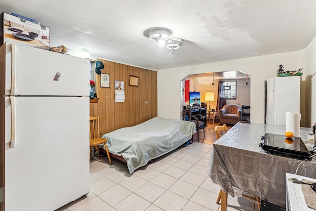 bedroom with wooden walls, light tile patterned floors, arched walkways, and freestanding refrigerator