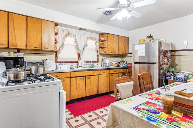 kitchen with light floors, white gas range oven, brown cabinets, freestanding refrigerator, and open shelves