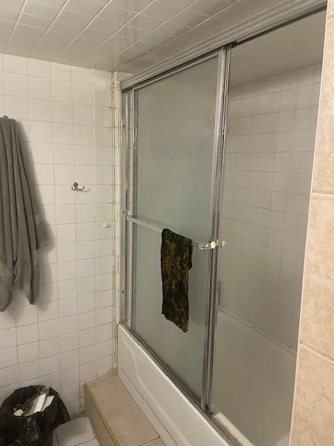 full bathroom featuring shower / bath combination with glass door, tile walls, toilet, and tile patterned floors