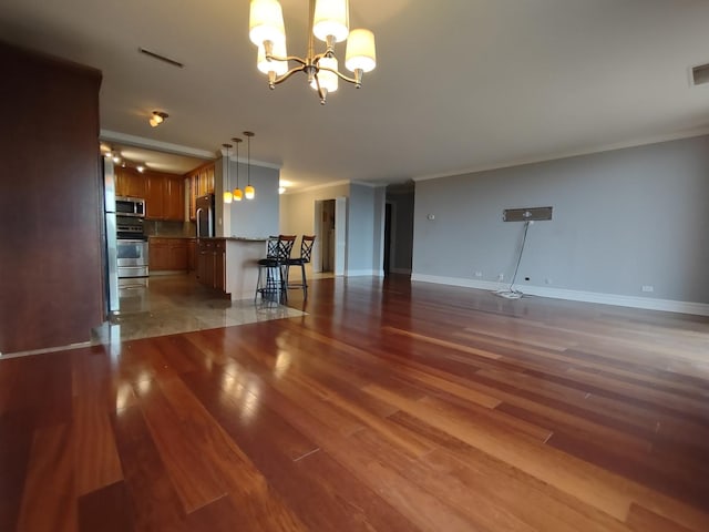 unfurnished living room featuring a notable chandelier, wood finished floors, visible vents, baseboards, and crown molding