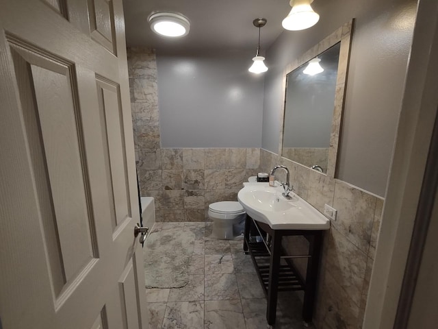 bathroom featuring toilet, a wainscoted wall, marble finish floor, vanity, and tile walls