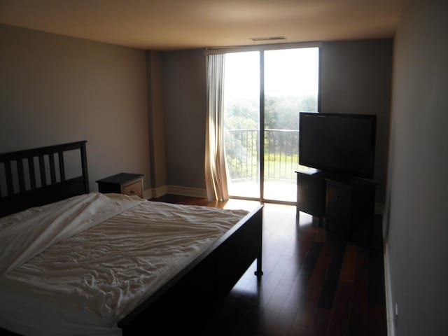 bedroom with floor to ceiling windows, visible vents, wood finished floors, access to outside, and baseboards