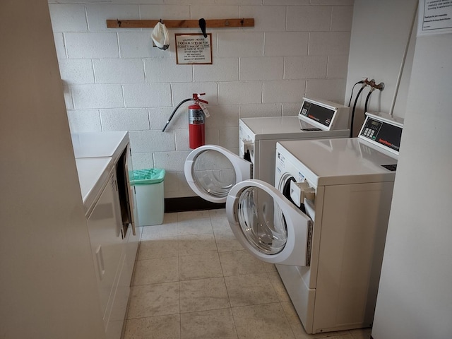 community laundry room featuring concrete block wall, separate washer and dryer, and light tile patterned flooring