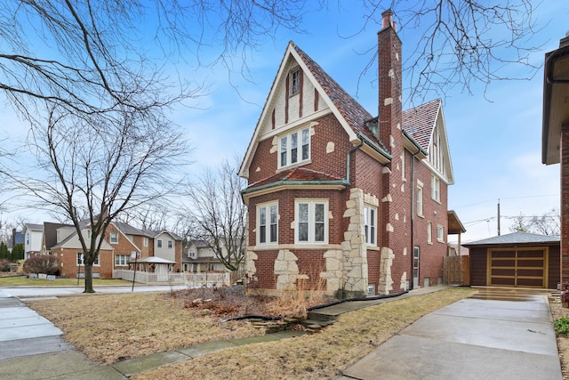 english style home featuring an outbuilding, a detached garage, a residential view, brick siding, and a chimney