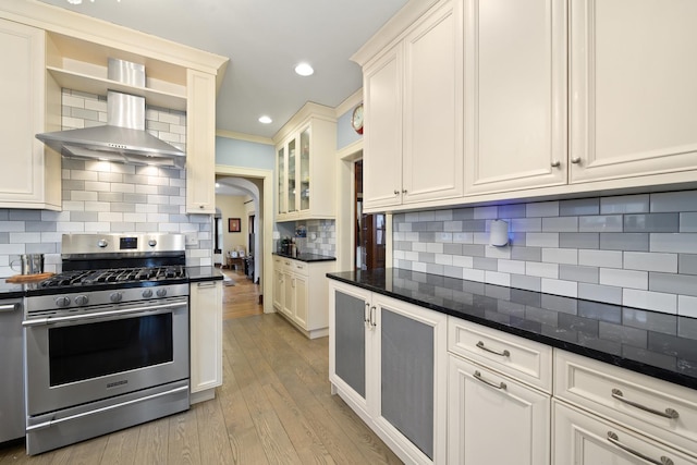 kitchen featuring light wood-type flooring, stainless steel gas stove, white cabinetry, arched walkways, and decorative backsplash