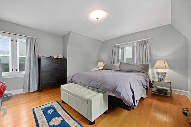 bedroom with vaulted ceiling, wood finished floors, and baseboards