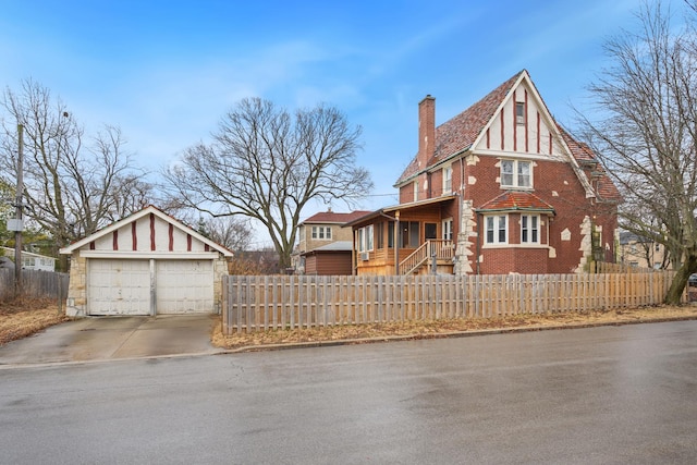 tudor house featuring a fenced front yard, an outdoor structure, a garage, brick siding, and a chimney