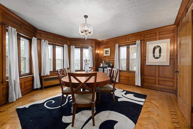 dining area featuring a notable chandelier, a textured ceiling, a decorative wall, and wooden walls