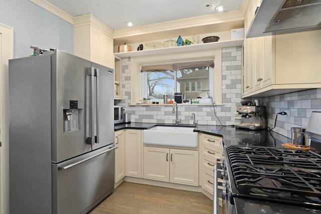 kitchen featuring light wood-style flooring, under cabinet range hood, a sink, dark countertops, and stainless steel appliances