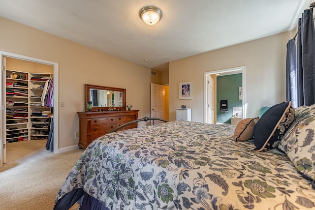 bedroom with visible vents, baseboards, a closet, a walk in closet, and light colored carpet