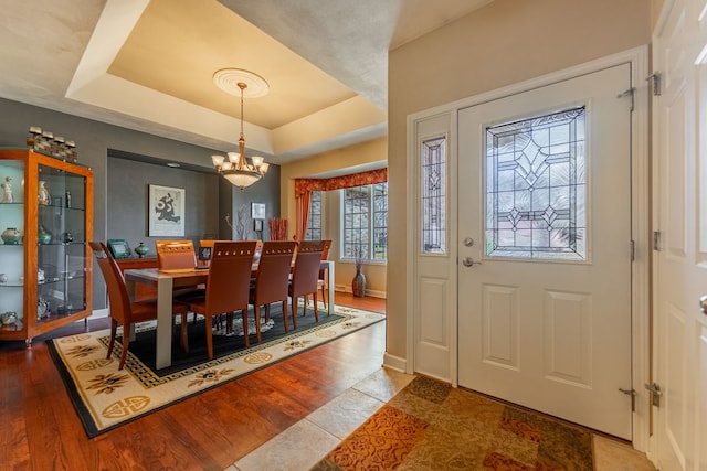 dining space with an inviting chandelier, a raised ceiling, wood finished floors, and baseboards