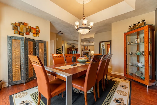 dining space featuring wood finished floors, baseboards, a tray ceiling, a fireplace, and a notable chandelier