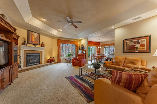 living area featuring visible vents, a ceiling fan, a tray ceiling, carpet floors, and a fireplace