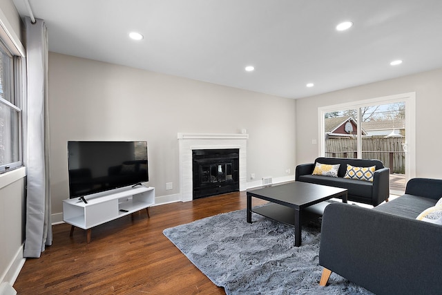 living room with visible vents, a glass covered fireplace, wood finished floors, recessed lighting, and baseboards