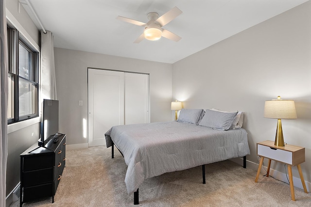 bedroom featuring a ceiling fan, light colored carpet, a closet, and baseboards