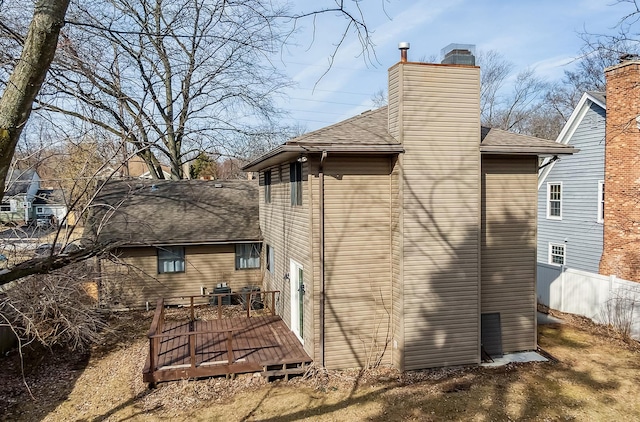 back of house featuring a chimney, a shingled roof, a deck, and fence