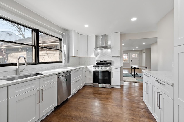 kitchen with dark wood finished floors, a sink, appliances with stainless steel finishes, wall chimney exhaust hood, and backsplash