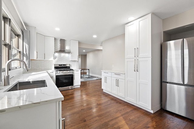 kitchen with light stone counters, dark wood-style floors, a sink, appliances with stainless steel finishes, and wall chimney exhaust hood