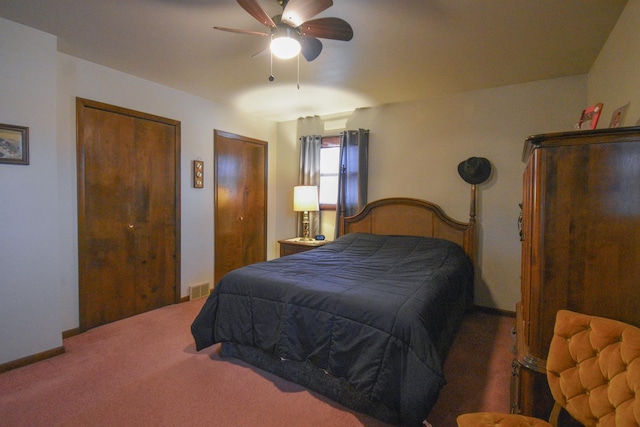 carpeted bedroom featuring multiple closets, visible vents, baseboards, and a ceiling fan