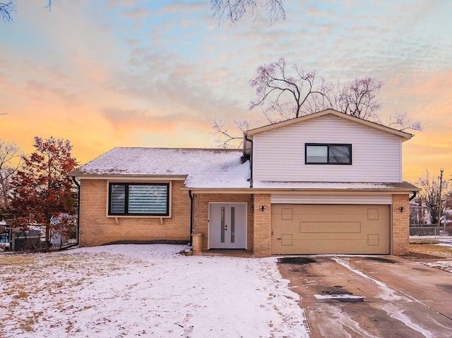 split level home with driveway, an attached garage, french doors, and brick siding