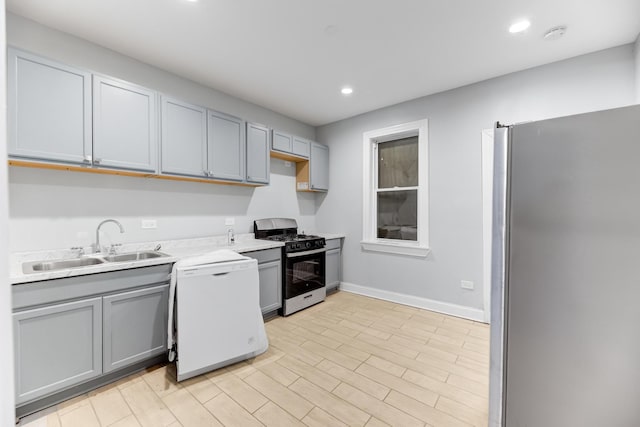 kitchen featuring baseboards, appliances with stainless steel finishes, light countertops, gray cabinetry, and a sink