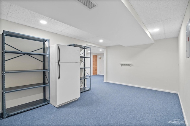 finished below grade area with visible vents, freestanding refrigerator, baseboards, carpet, and a paneled ceiling