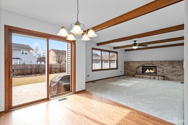 unfurnished living room with visible vents, a brick fireplace, baseboards, beamed ceiling, and wood finished floors