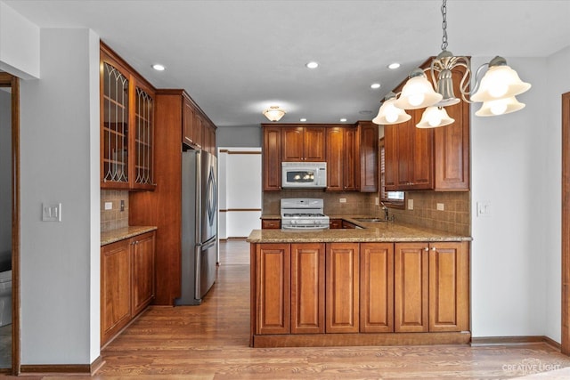 kitchen with brown cabinetry, white appliances, light wood-type flooring, and glass insert cabinets